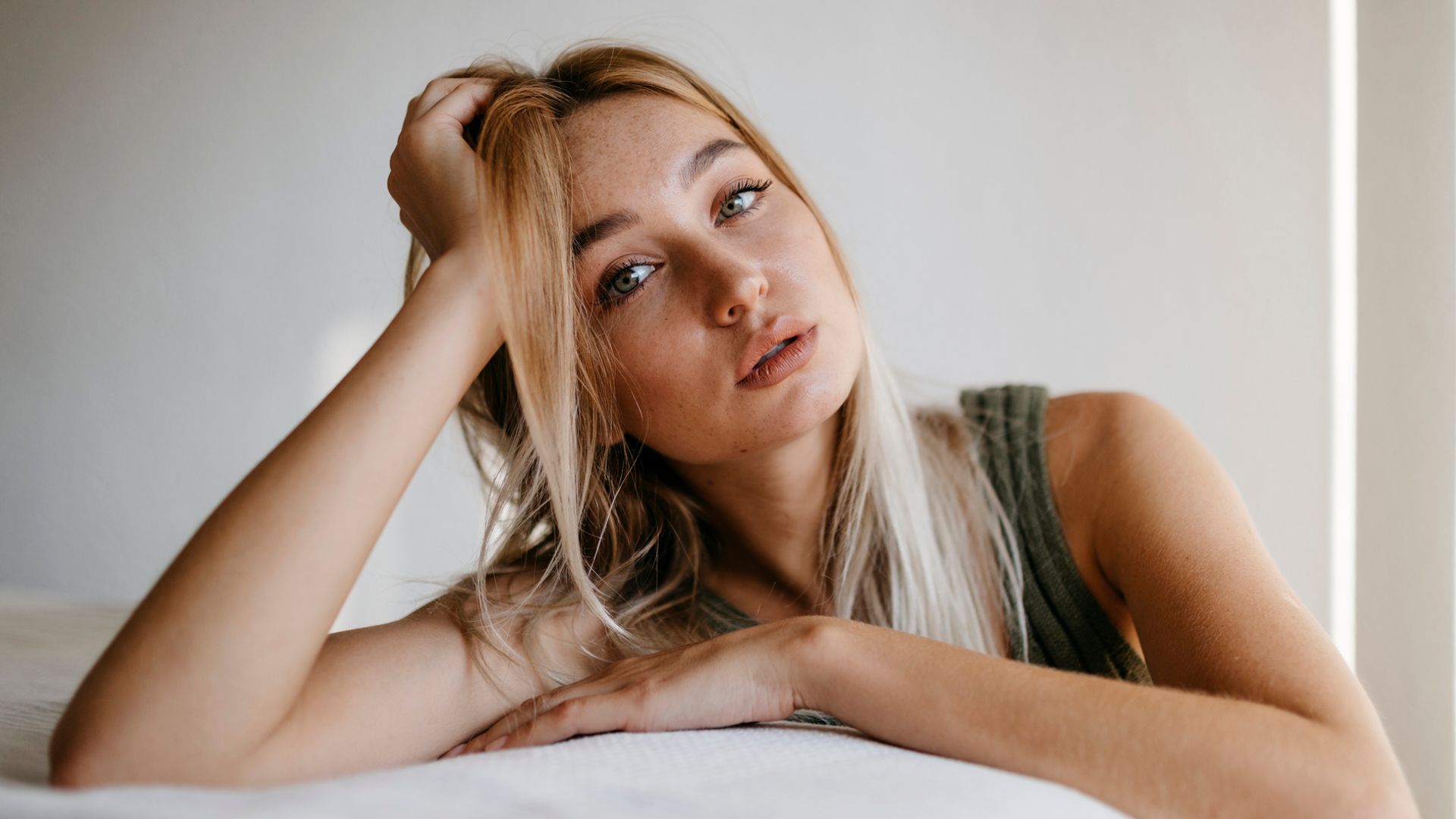 Mujer apoyada en los pies de la cama con el rostro serio