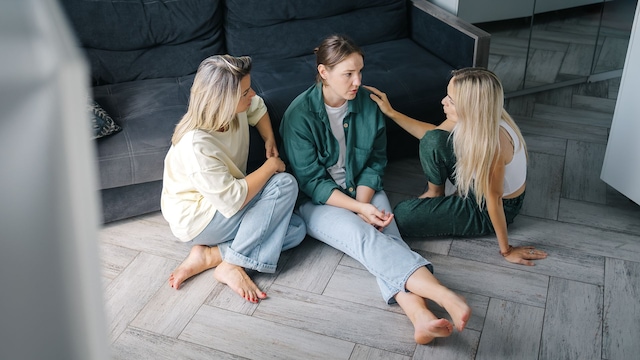 amigas hablando, sentadas en el suelo, ayudando a una de ellas con problemas