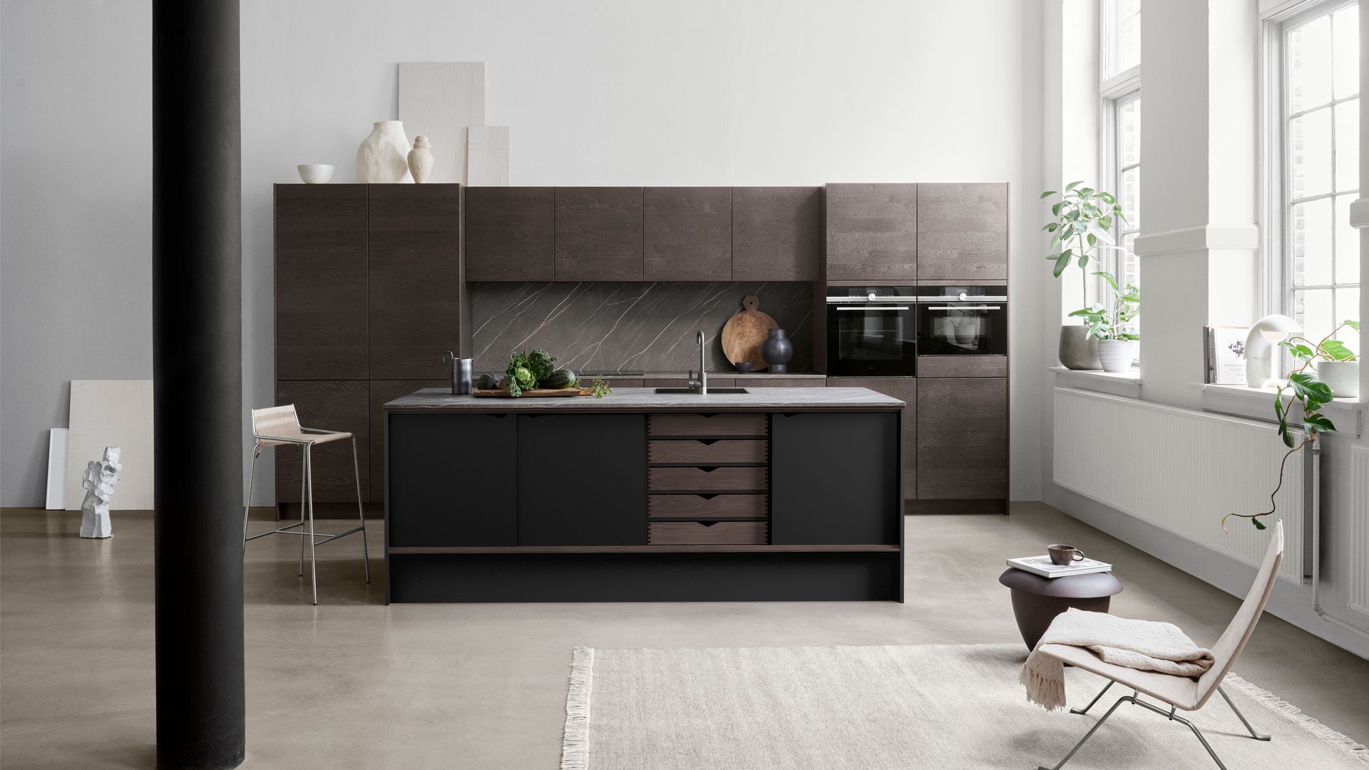 Cocina XL con muebles de madera oscura, gran ventanal, radiador, alféizar con plantas, cocina con isla, alfombra, butaca