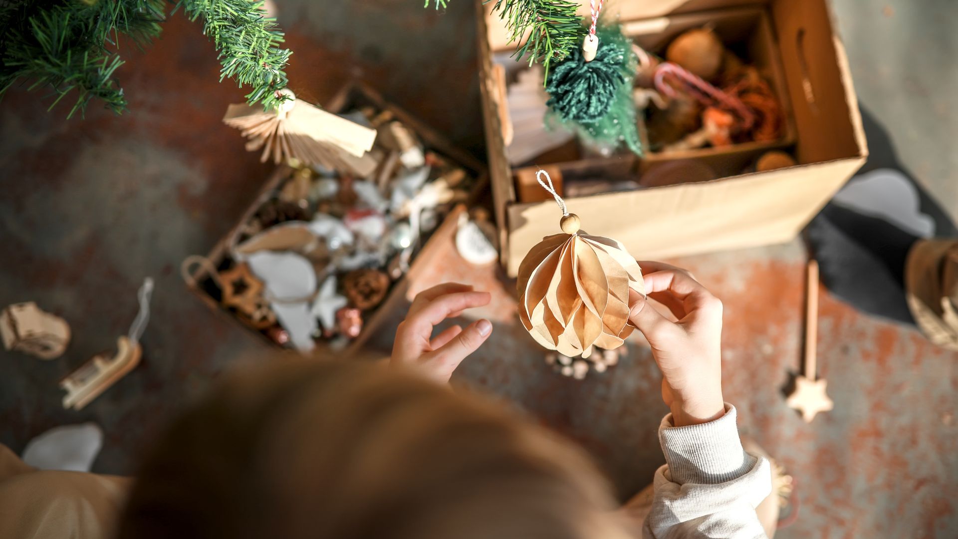 Niño sujetando adornos navideños mientras decora el árbol de Navidad, con una visión cenital.