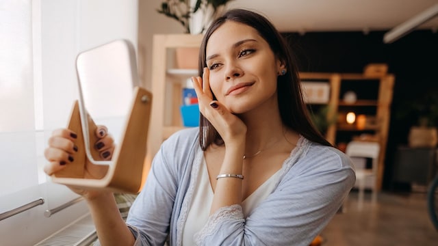 Mujer mirándose el rostro en un espejo de mano