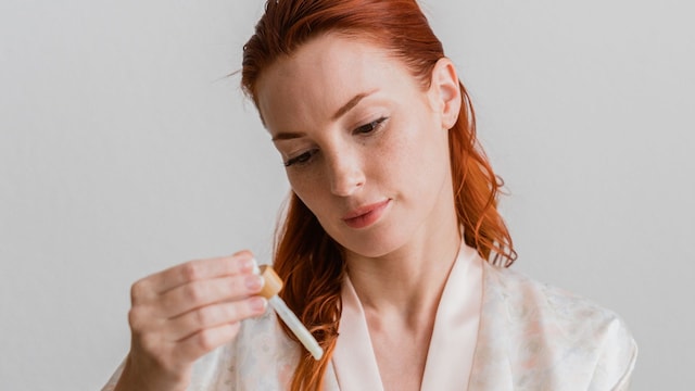 Mujer pelirroja aplicando sérum facial en sus manos