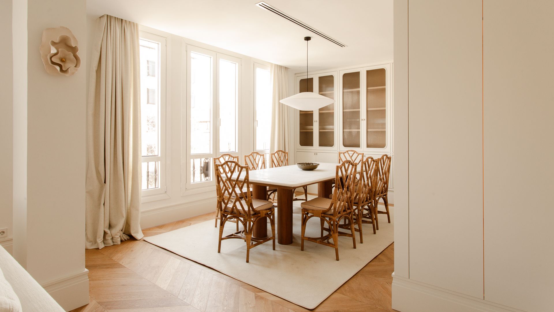 Comedor con grandes ventanales blancos, alfombra, vitrina, cortinas mesa de centro de madera, sillas de madera 