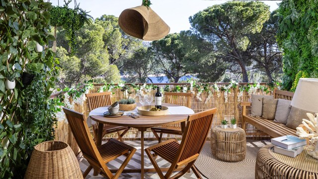 Terraza con mesa de comedor redonda, sillas de madera, alfombra, banco, mesas de centro de fibras vegetales y plantas