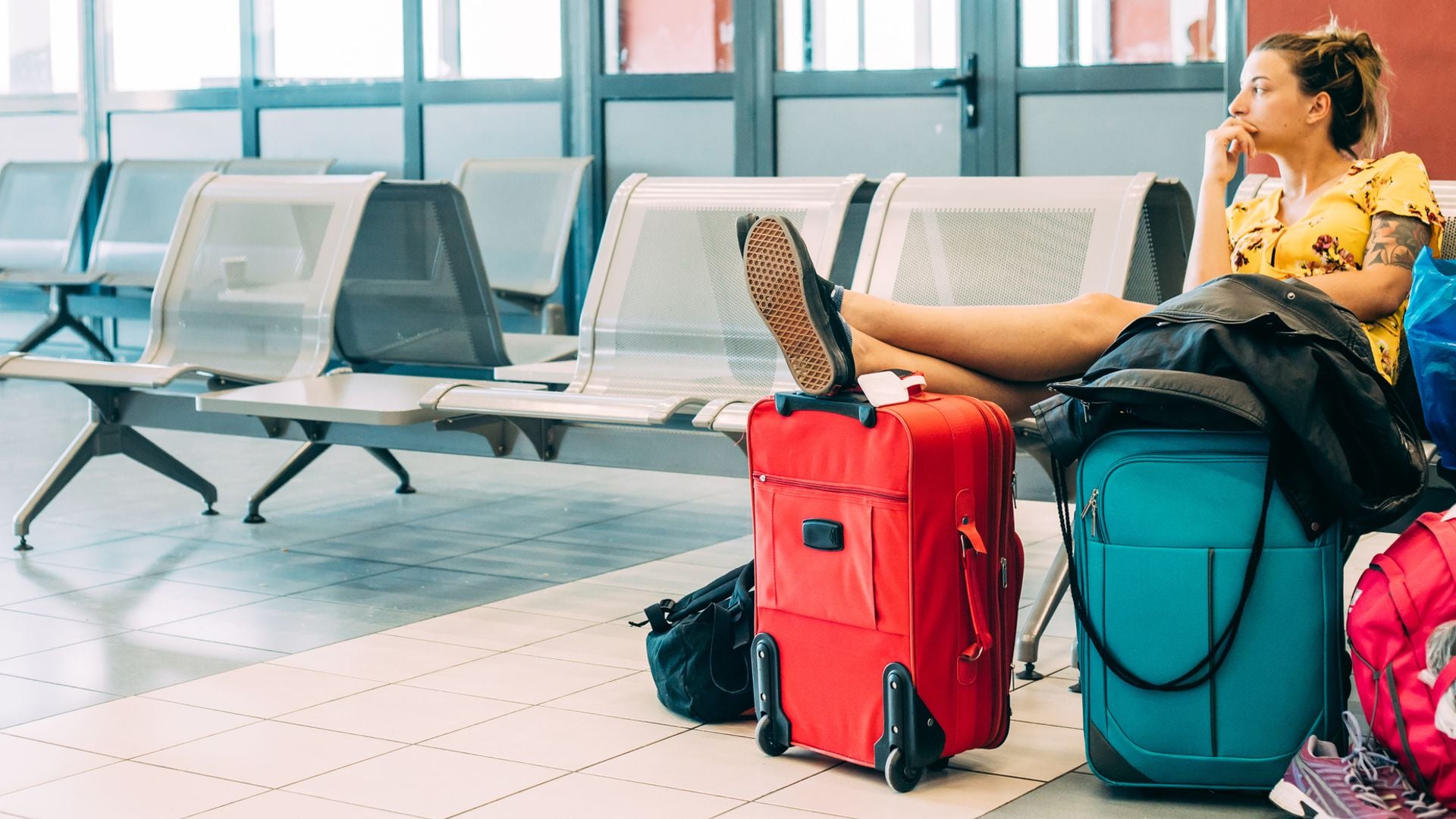 Mujer joven esperando en la sala de espera de una estación de tren con maletas y mochilas.