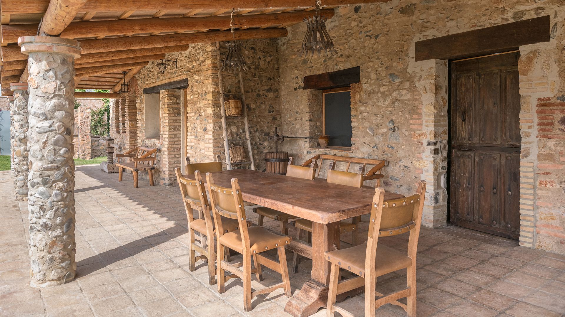 Porche de casa de campo con paredes de piedra, puertas de madera, comedor exterior 