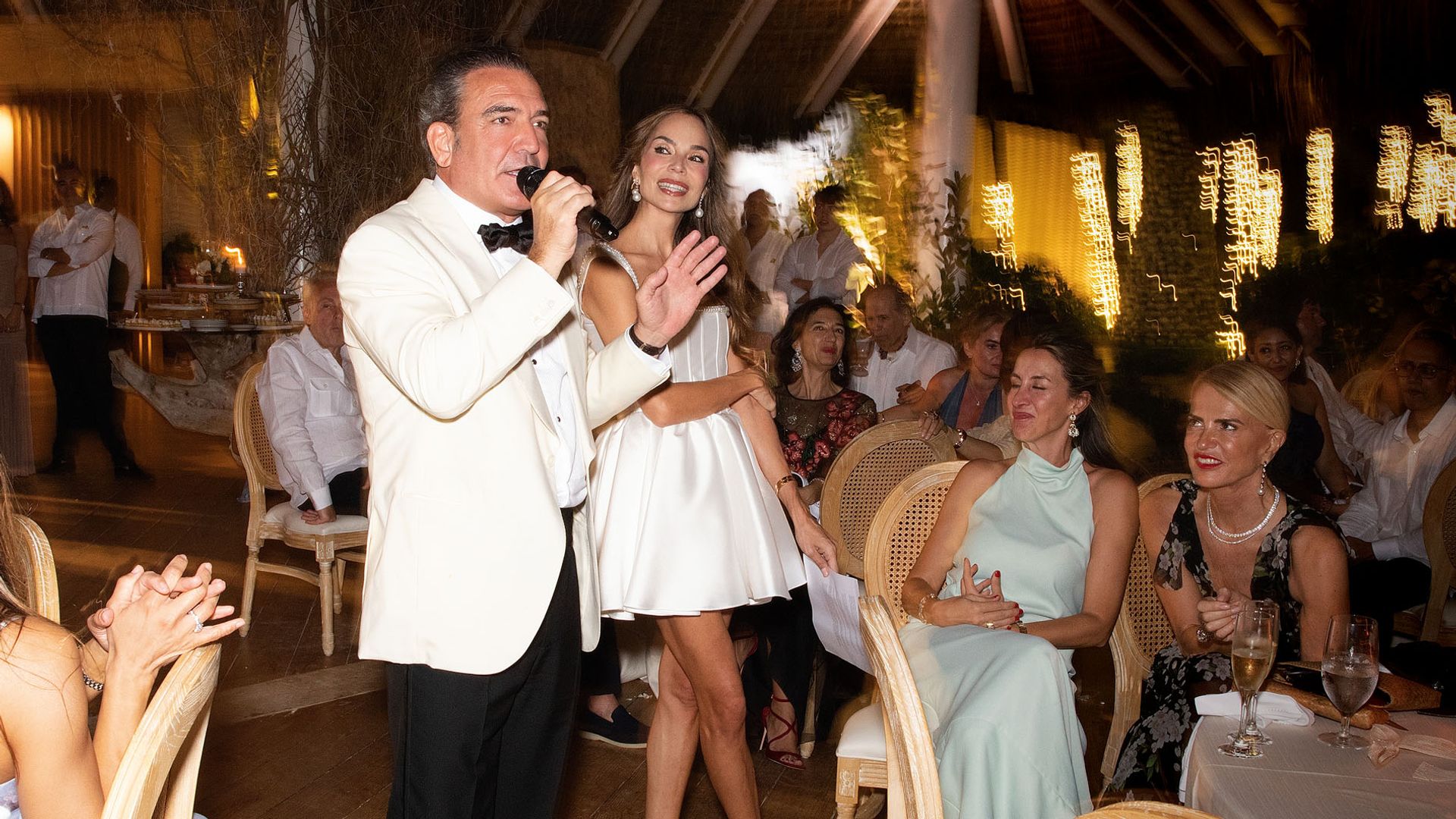 Hombre en smoking y mujer en vestido cantando en un evento social nocturno.