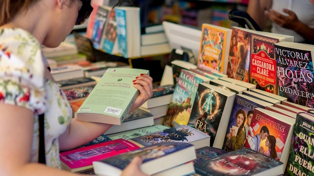 Una mujer leyendo libros en uno de los puestos de la Feria del Libro de Madrid.