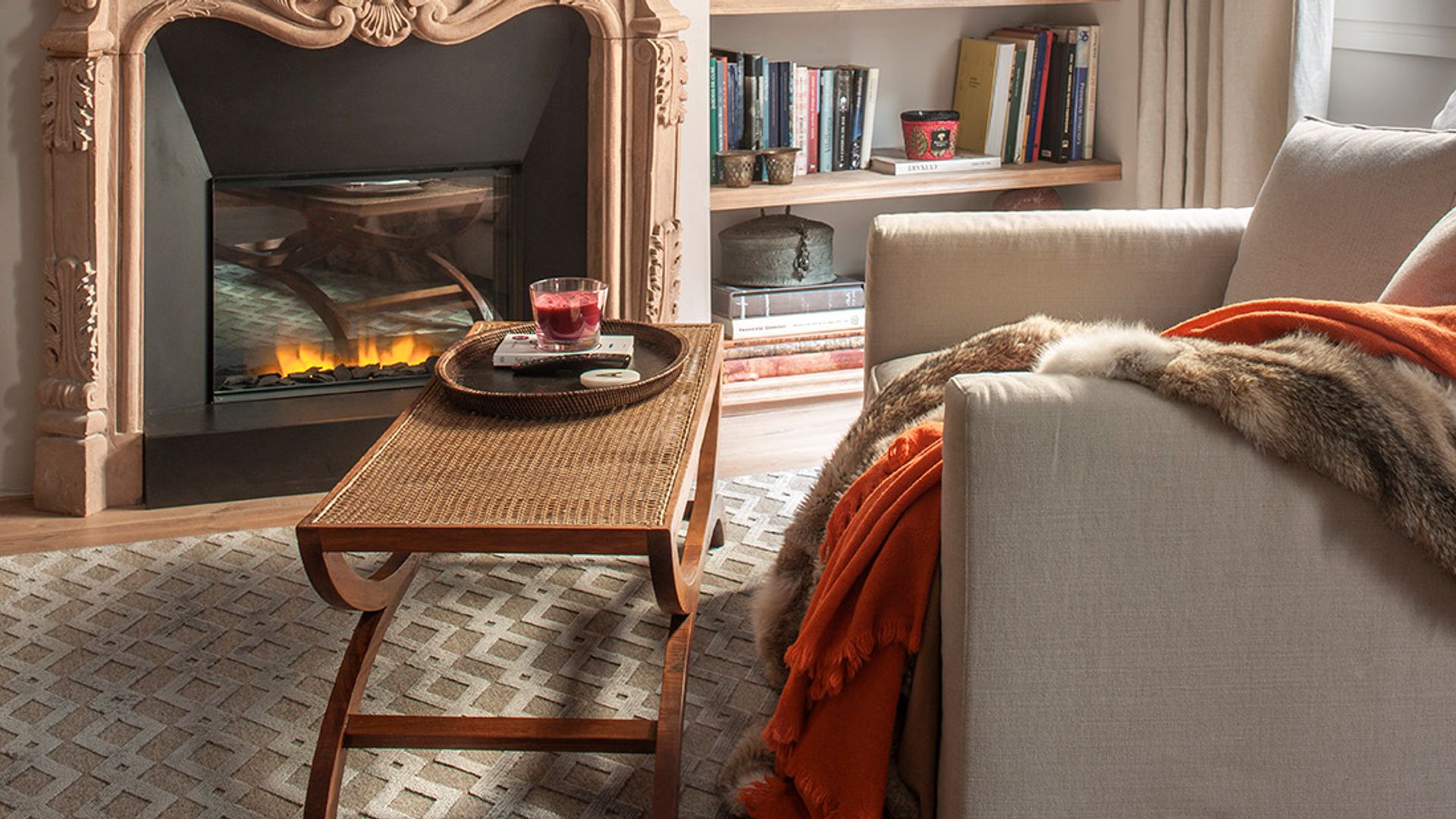 Salón con chimenea, estantería en hornacina con baldas de madera, butaca, mesa de rejilla, mantas sobre la butaca 