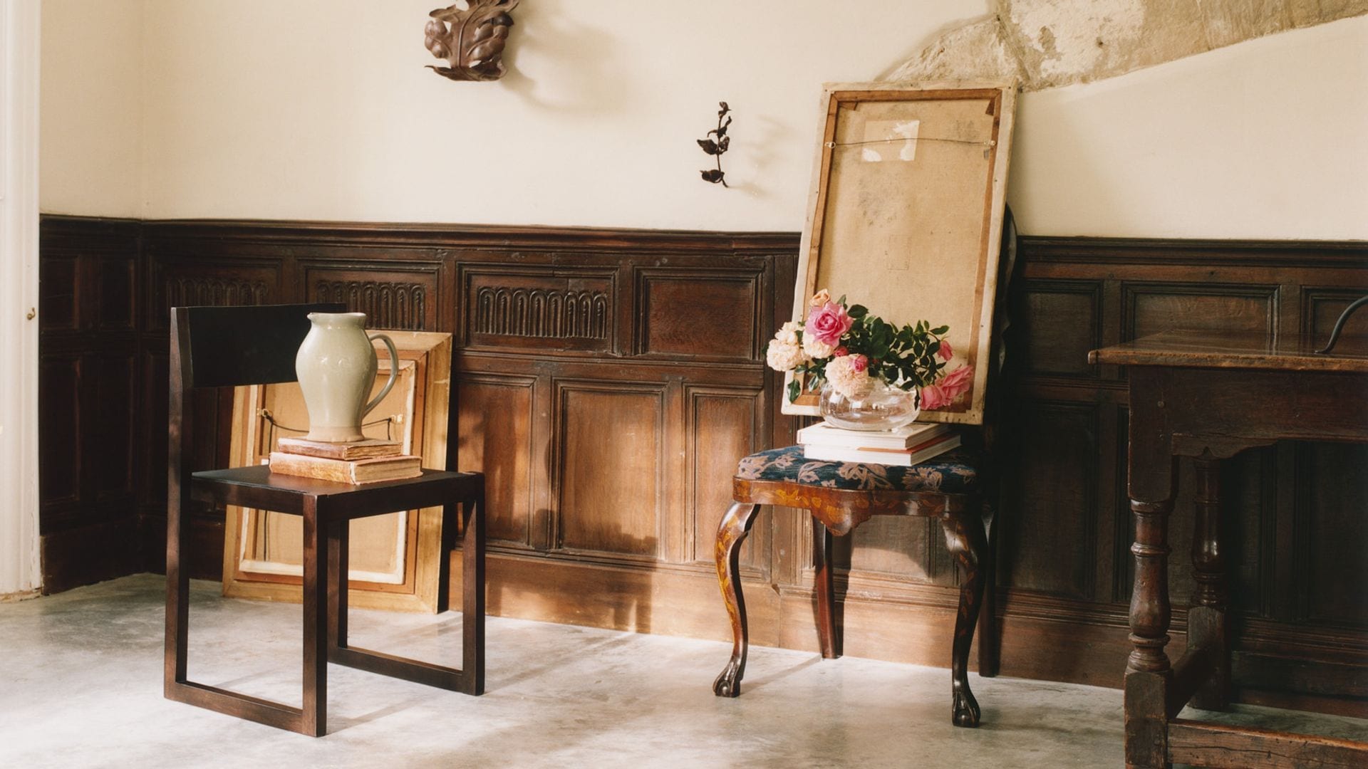 Recibidor antiguo con zócalo alto de madera oscura, silla de madera, oscura, aparador, pintura, jarrón con flores, jarrón de porcelana