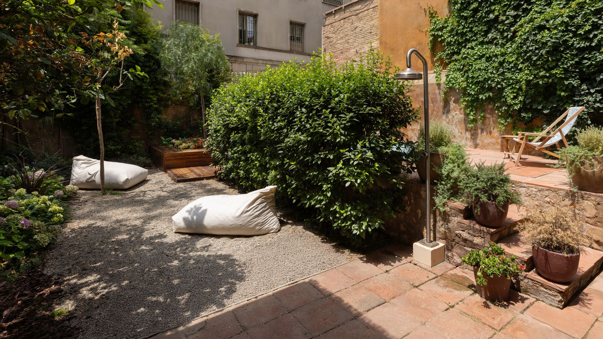 Patio con piscina, suelo de barro, árboles y enredaderas verdes, ducha exterior