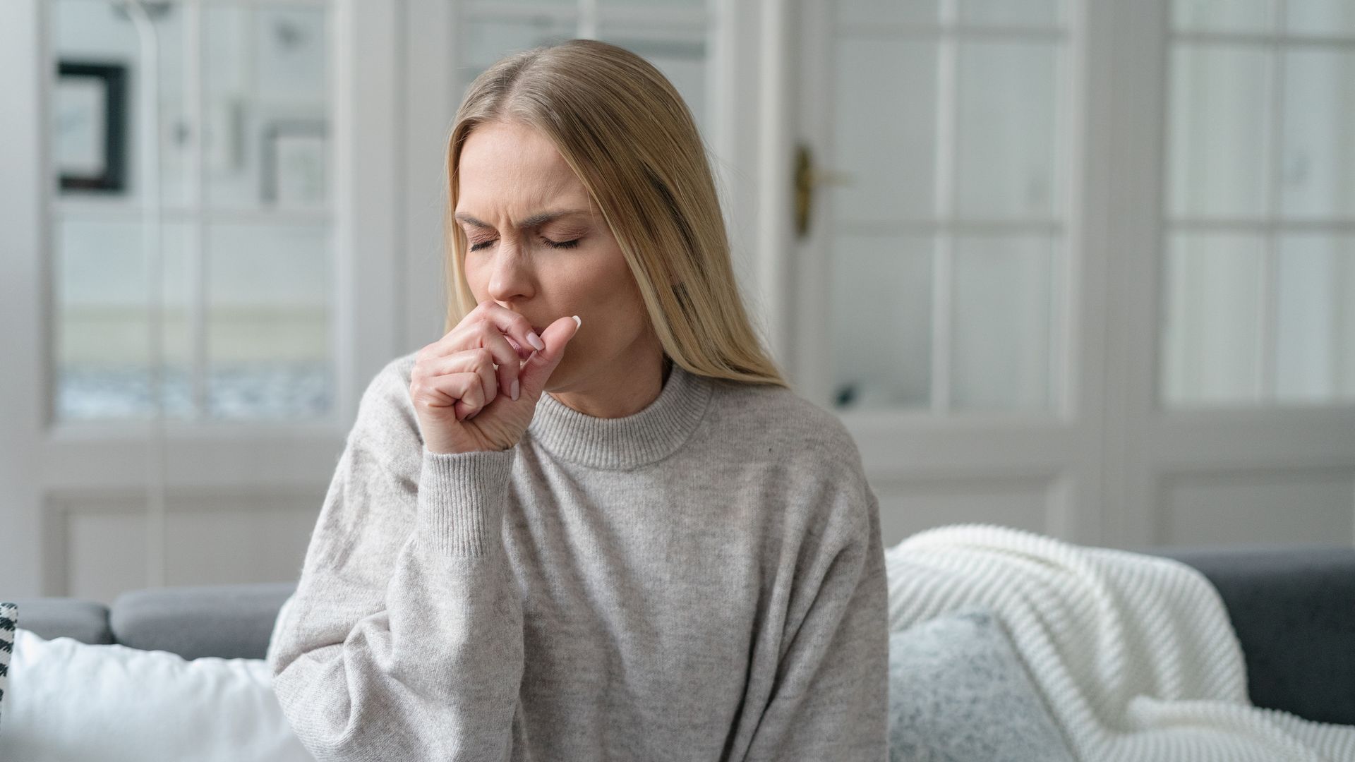 mujer tosiendo, sentada en el sofá de su casa