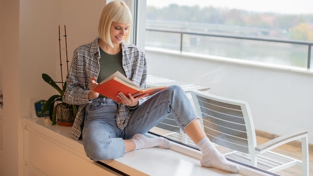 Mujer leyendo un libro al lado de una ventana