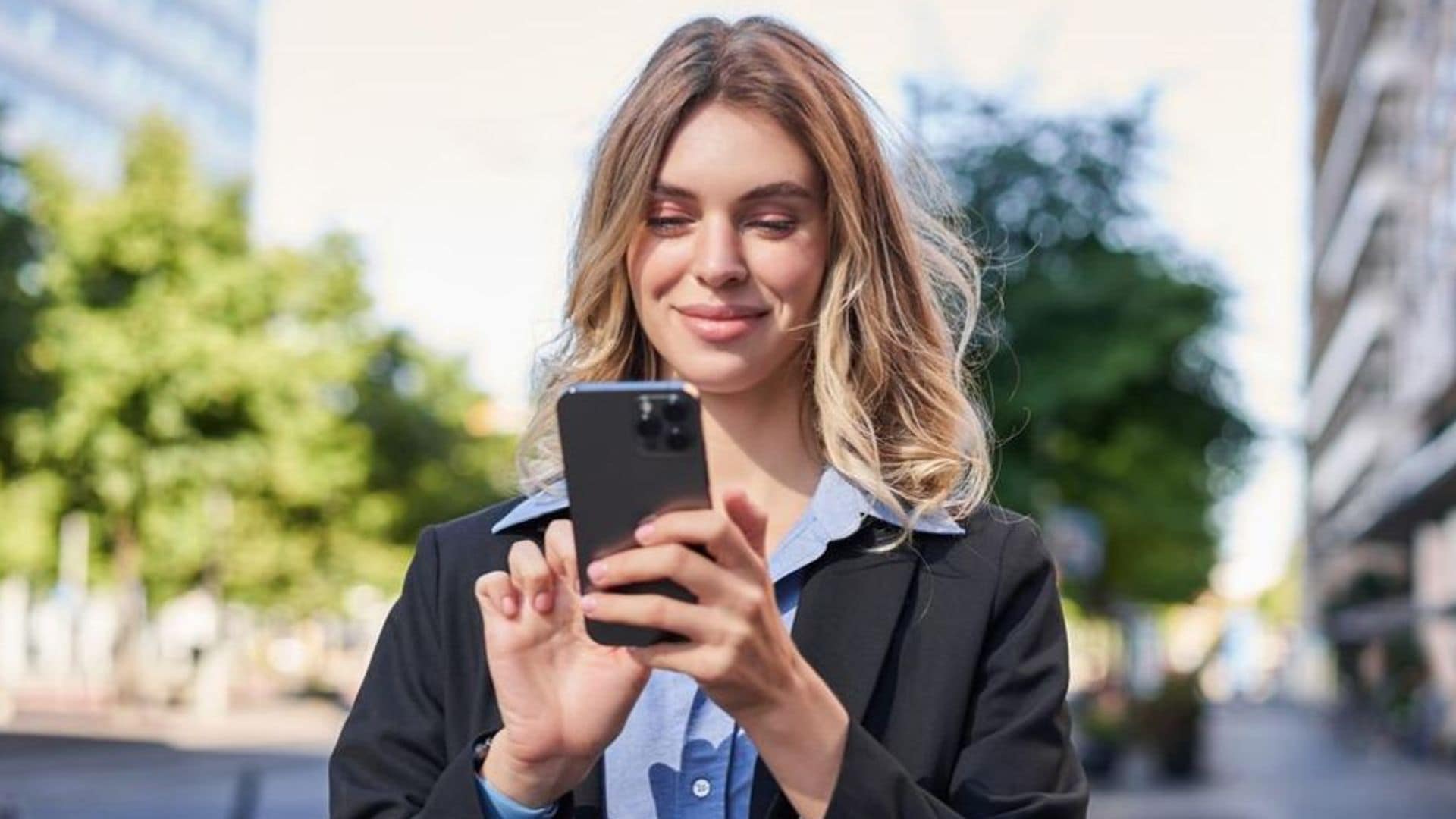Mujer rubia joven en la calle mirando su teléfono móvil
