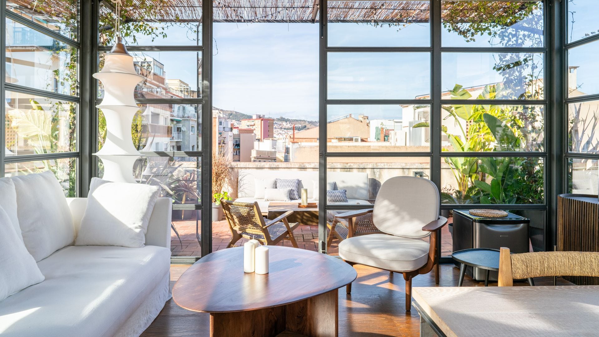 Salón conectado con la terraza de un ático con vistas edificios, puertas de cristal con cuarterones metálicos