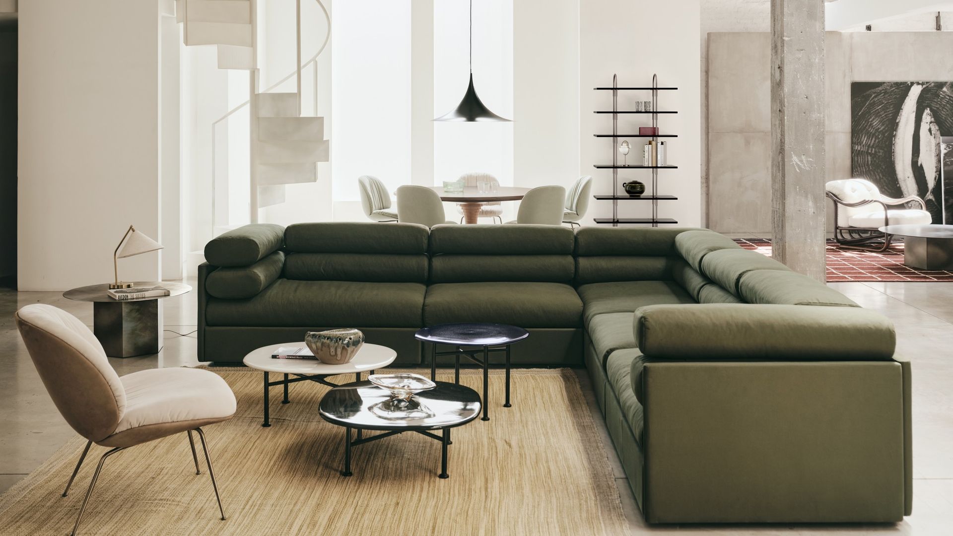 Salón comedor con sofá verde, mesas de centro, alfombra, butaca beige, escalera y mesa de comedor redonda