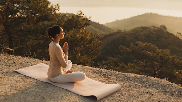 Mujer practicando Hatha Yoga en lo alto de la montaña sobre una esterilla al atardecer