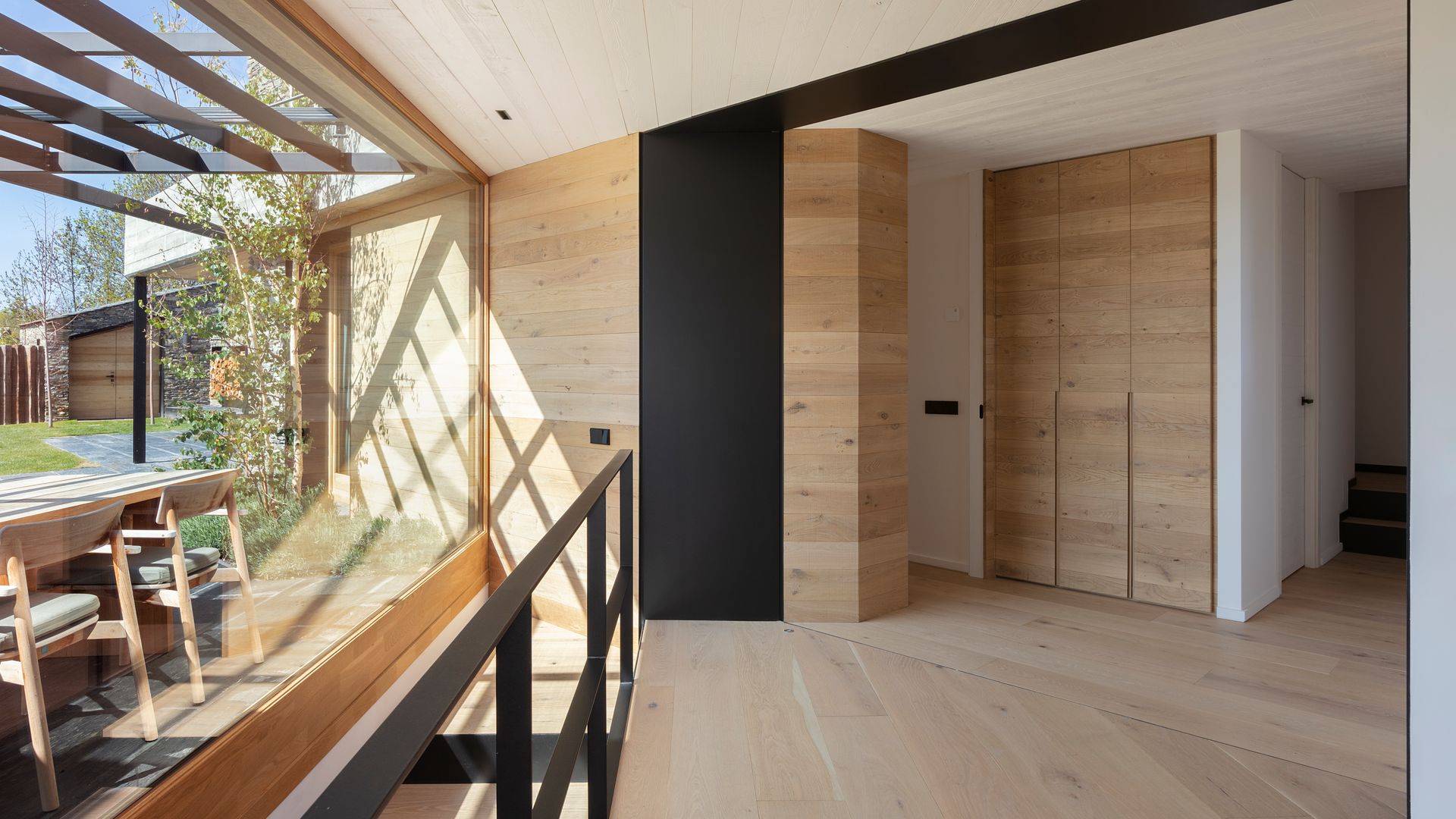 Recibidor con armario de madera, suelo de madera, gran ventanal con vistas al comedor exterior, techo de madera blanco 