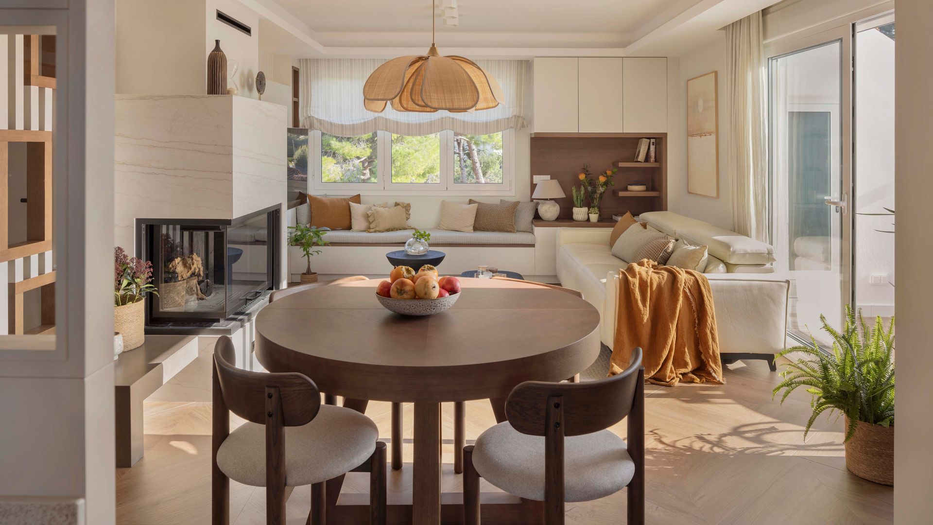 Salón comedor con chimenea, mesa redonda de madera oscura, sillas de madera con asiento tapizado blanco, sofá blanco, suelo en espiga 