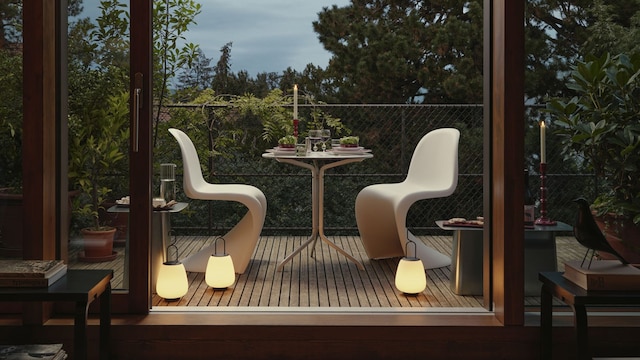 Terraza con suelo de madera, sillas Panton blancas, lámparas portátiles encendidas, mesa con candelabro