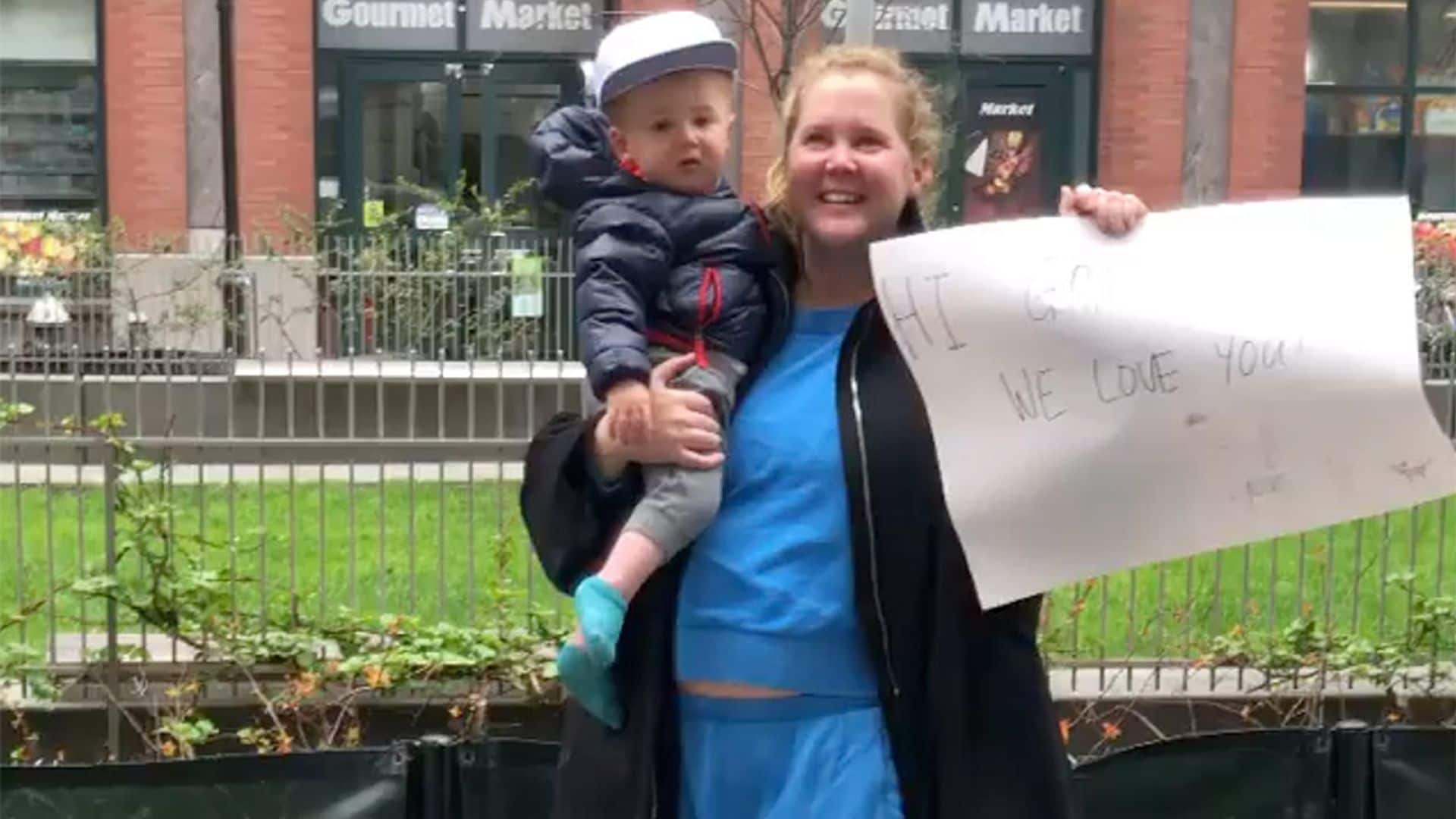 Con su hijo en un brazo y un cartel en otro, Amy Schumer envía ánimos a su padre desde la acera