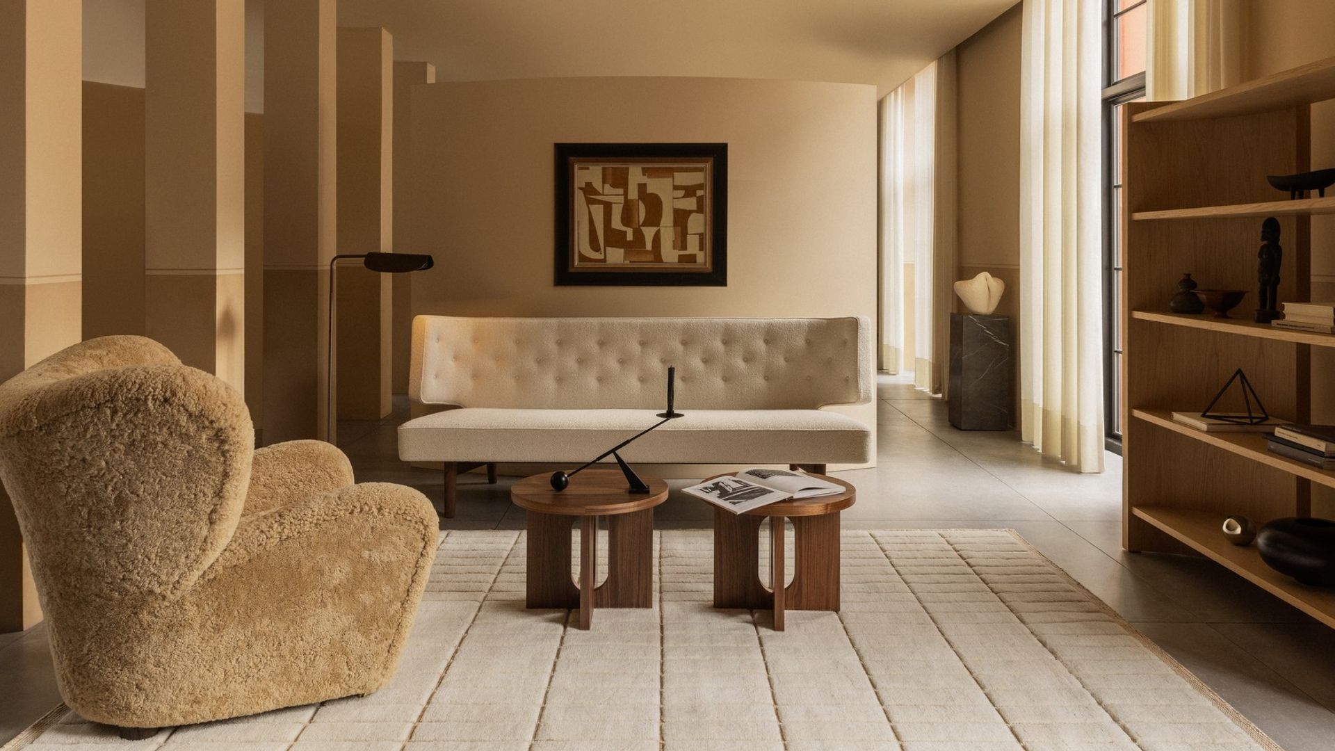 Salón en tonos beiges con butaca de pelo, sofá con capitoné, mesas de madera, cortinas y columnas 