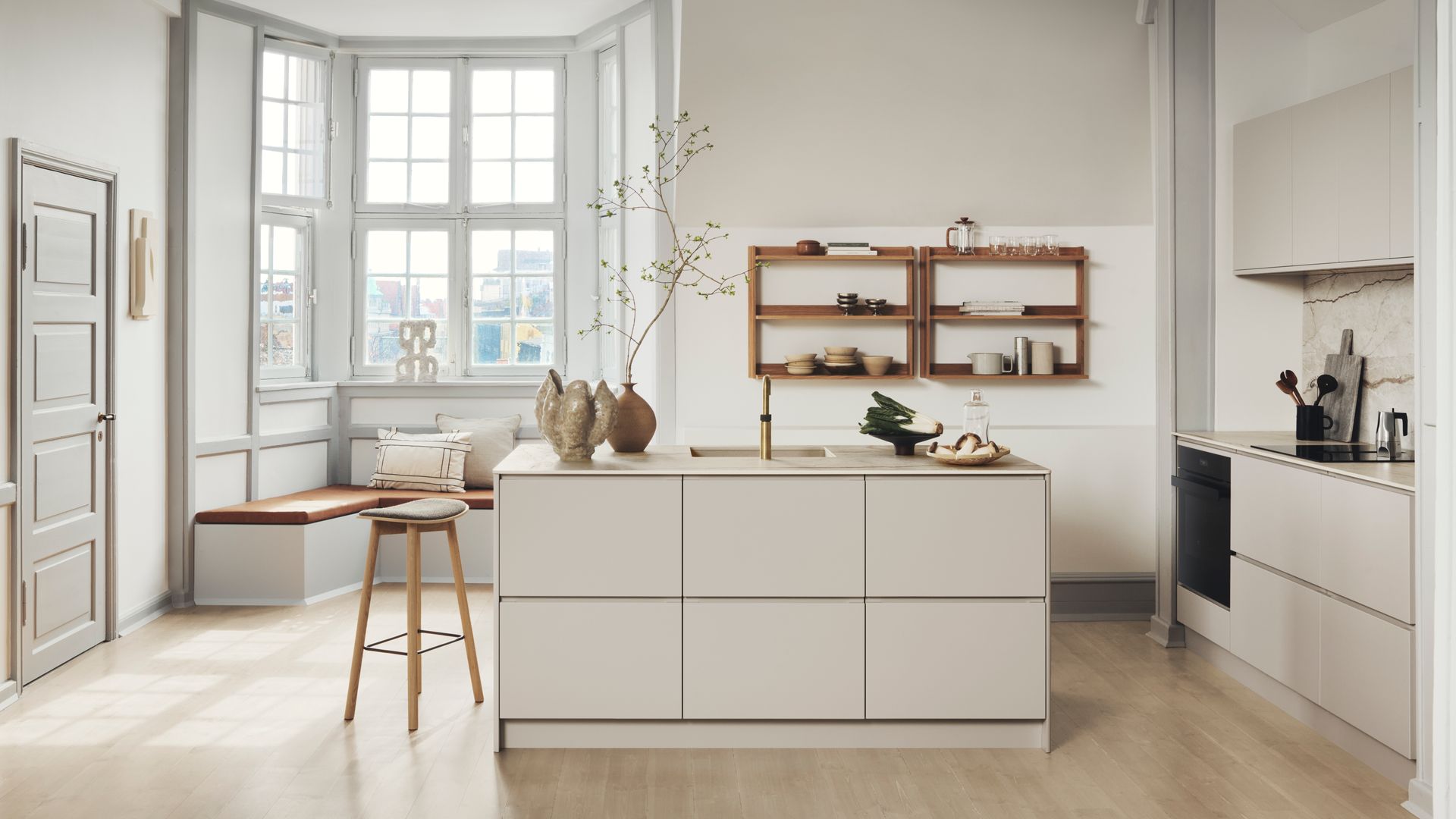 Cocina crema con isla, banco bajo la ventana, suelo de madera, estantería de madera