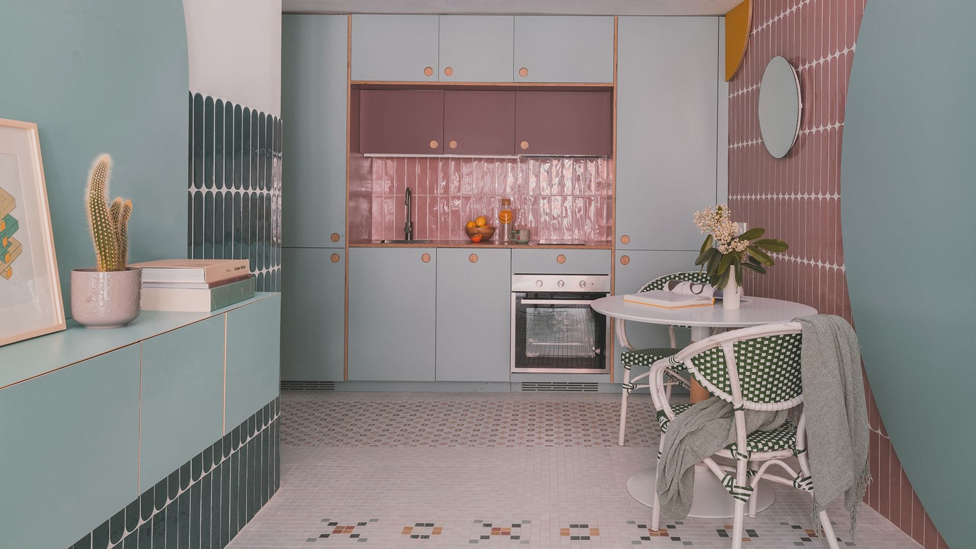 Cocina IKEA en azul cielo con armarios hasta el techo, sin tiradores, mesa de comedor redonda, sillas antiguas en verde y blanco, paredes de azulejos, suelo porcelánico