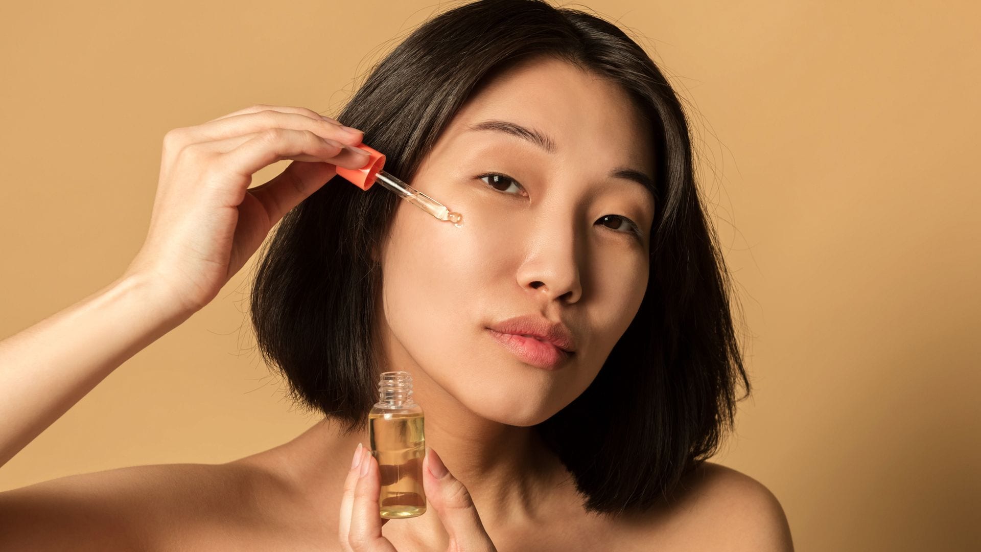 Mujer joven asiática aplicándose sérum facial en el rostro con pipeta