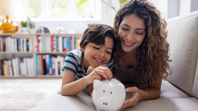 Madre con su hijo en el sofá de su casa ahorrando dinero con una hucha
