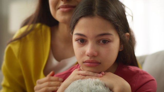 Niña triste y deprimida se sostiene sobre un peluche mientras su madre la abraza