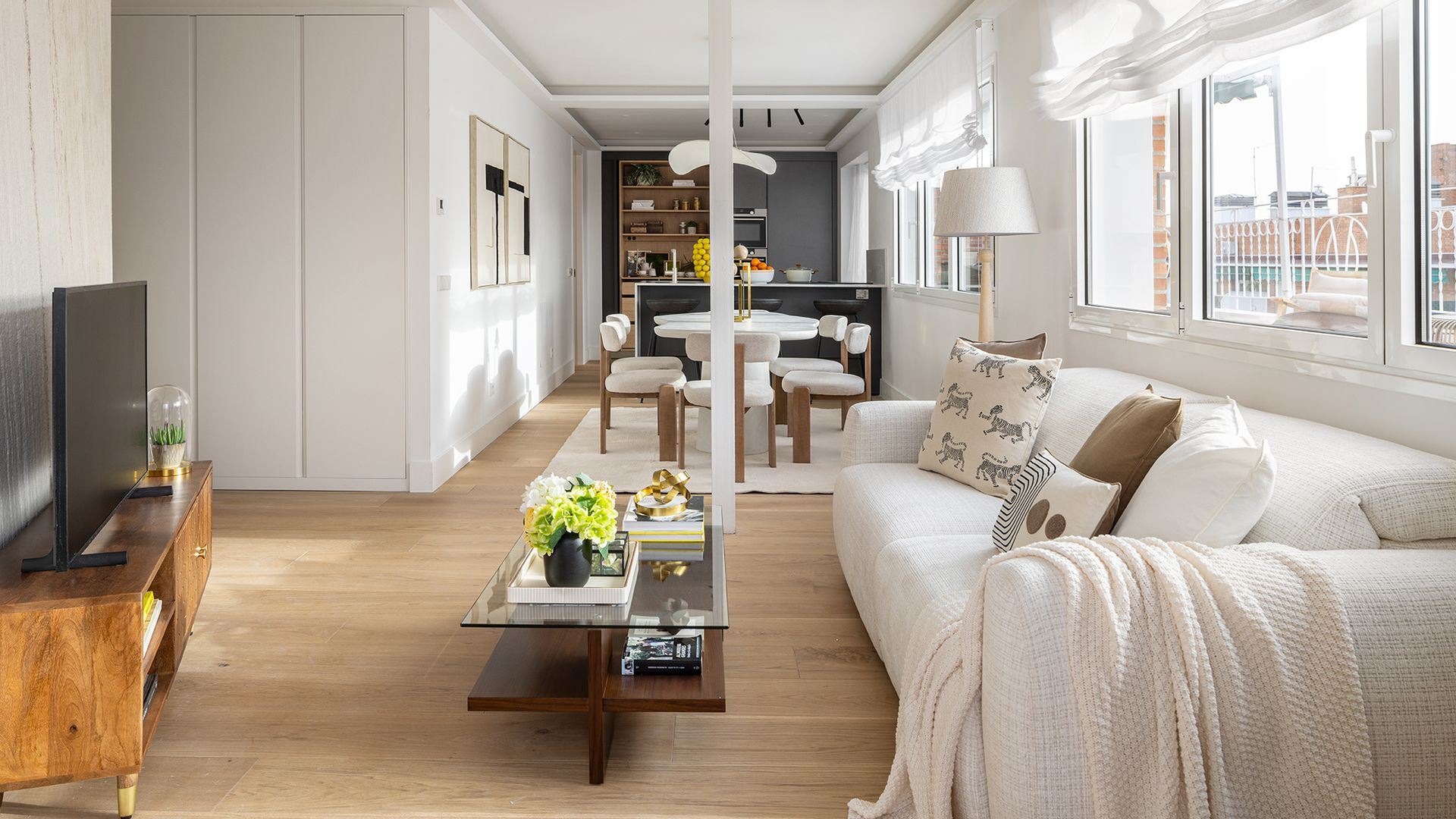 Salón, comedor y cocina con grandes ventanales con vistas de la terraza, estores blancos, sofás blancos