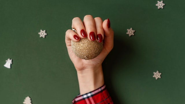 Mano de mujer agarrando una bola para el árbol con manicura roja de Navidad