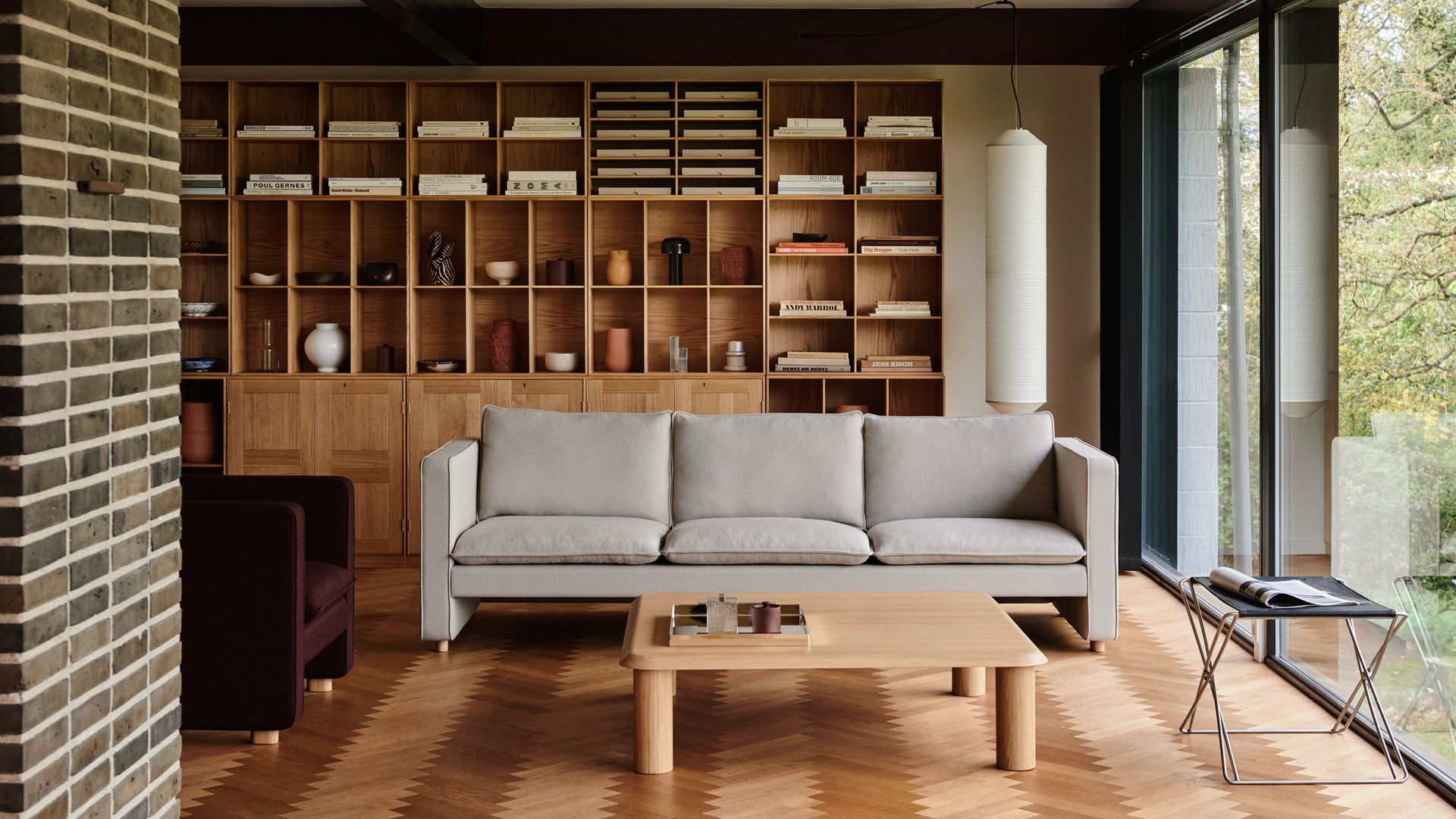 Salón con estantería de madera con puertas en la parte inferior y estantes abiertos en la superior, sofá gris, mesa de centro de madera y suelo de madera 