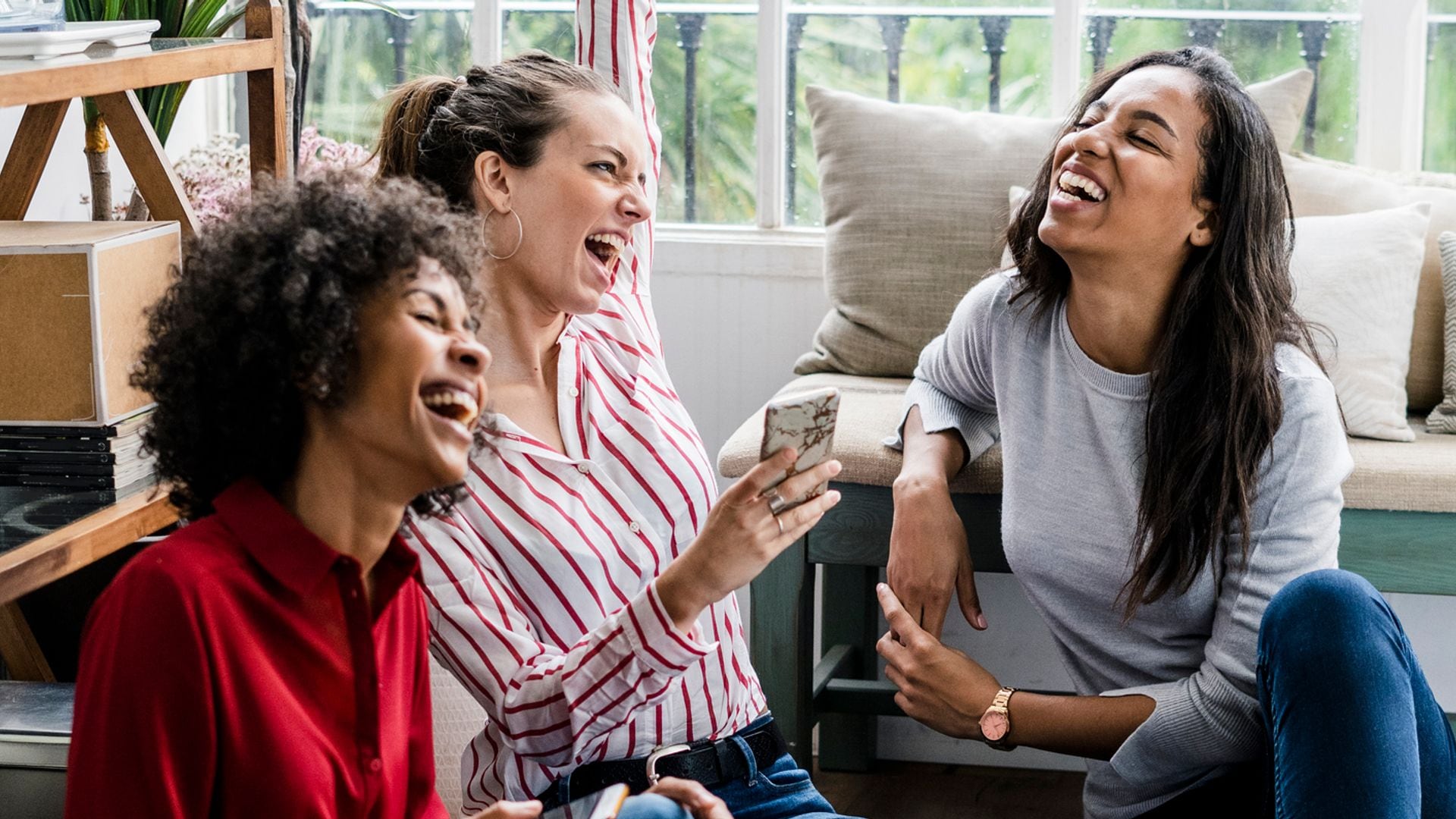 tres amigas sentadas en el suelo de casa, muy sonrientes y felices