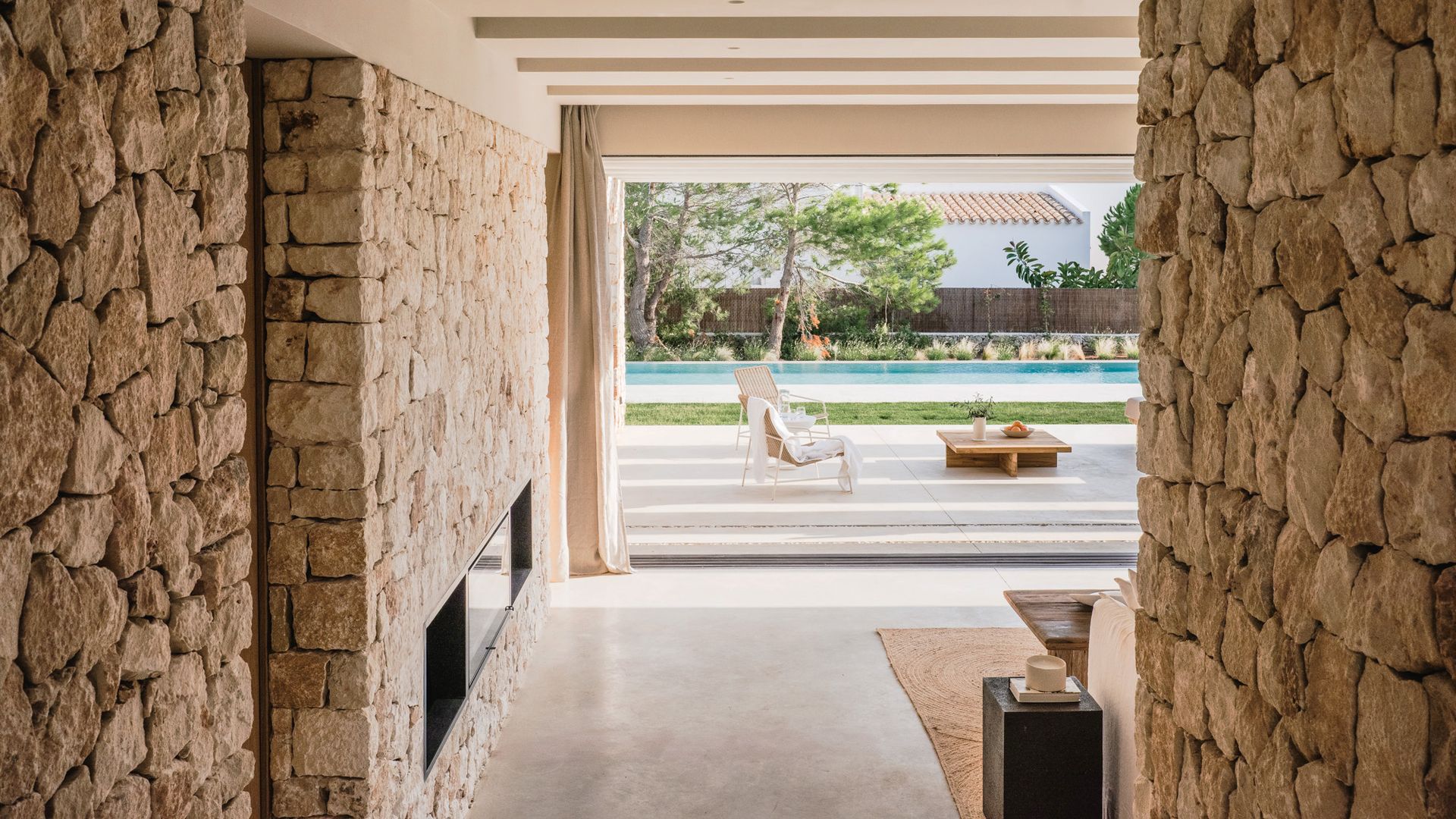 Salón con chimenea, pared de piedra y salida a la piscina 