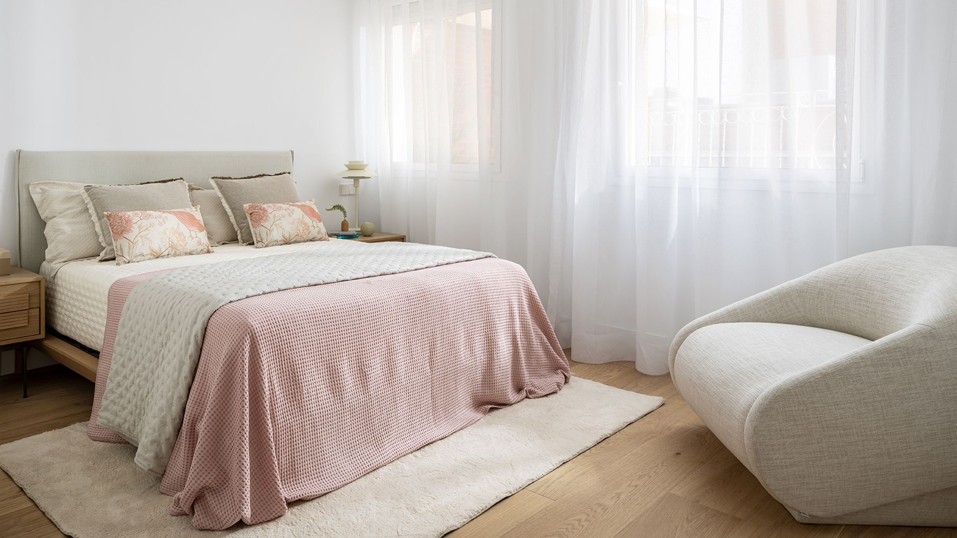 Dormitorio principal con cortinas blancas, alfombra, ropa de cama rosa claro, butaca, cabecero tapizado