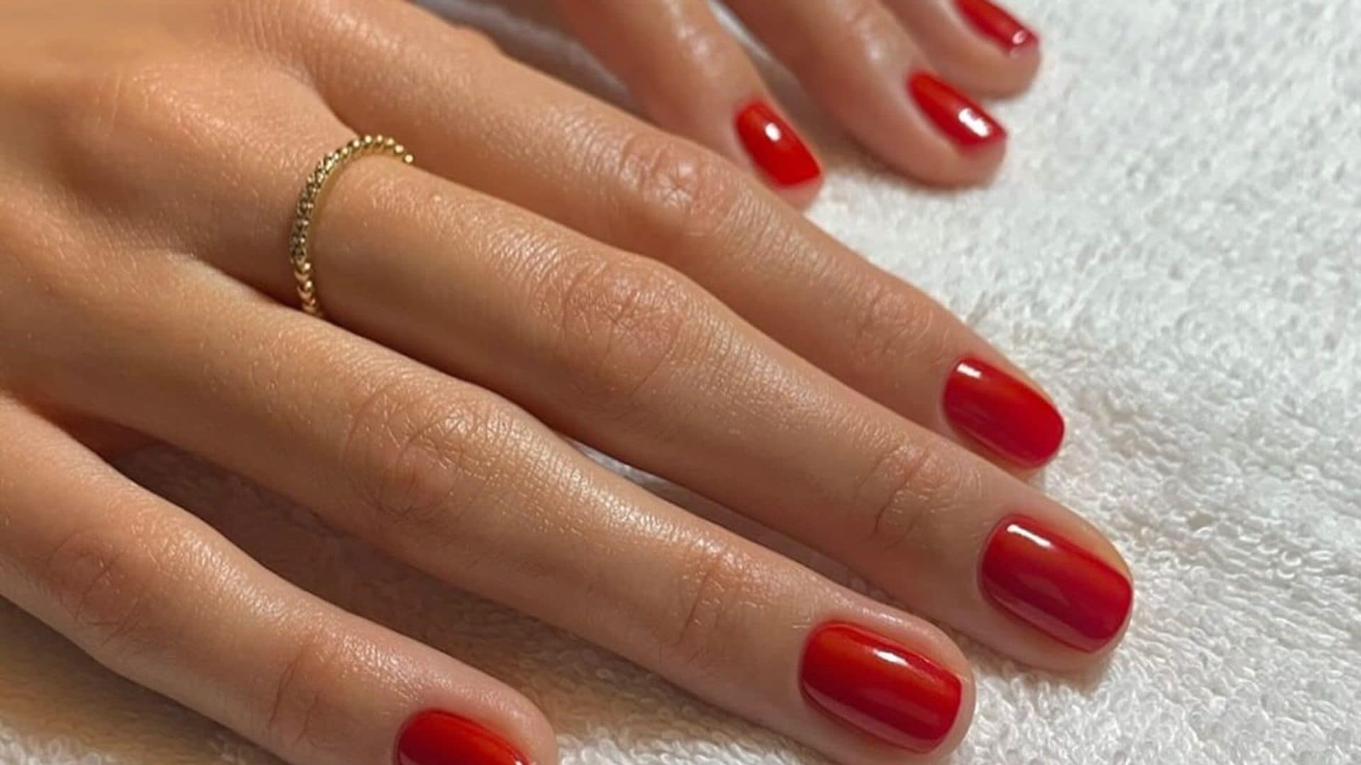 Manos con manicura roja sobre una mesa con vaso de cristal de fondo