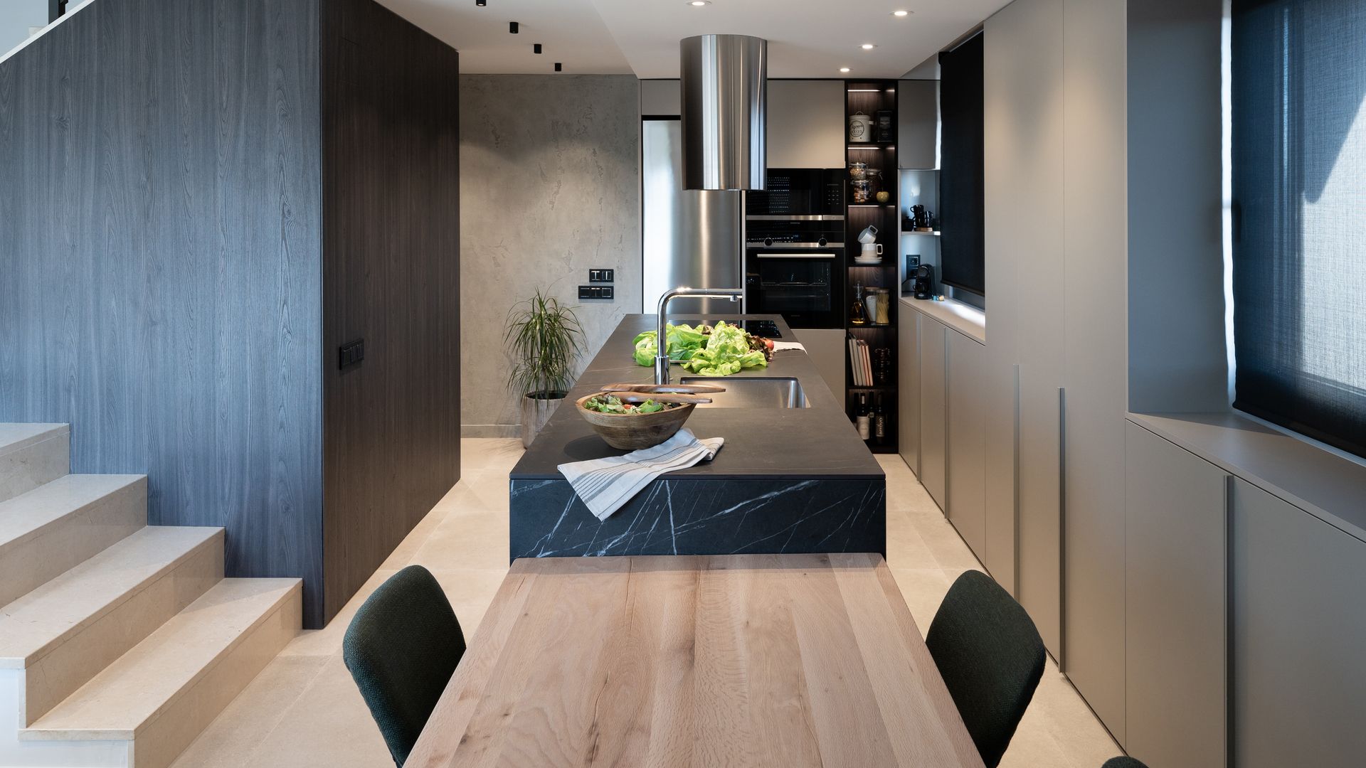 Cocina negra con isla de cocina, campana decorativa, mesa de madera adosada a la isla 