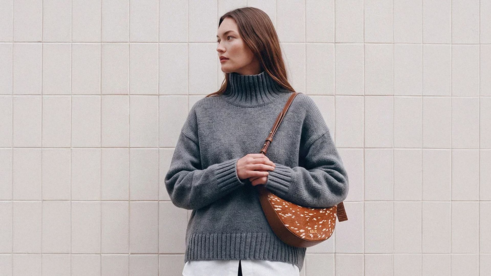 Mujer con jersey de punto gris, pantalón negro y bolso con estampado bambi de Kalk