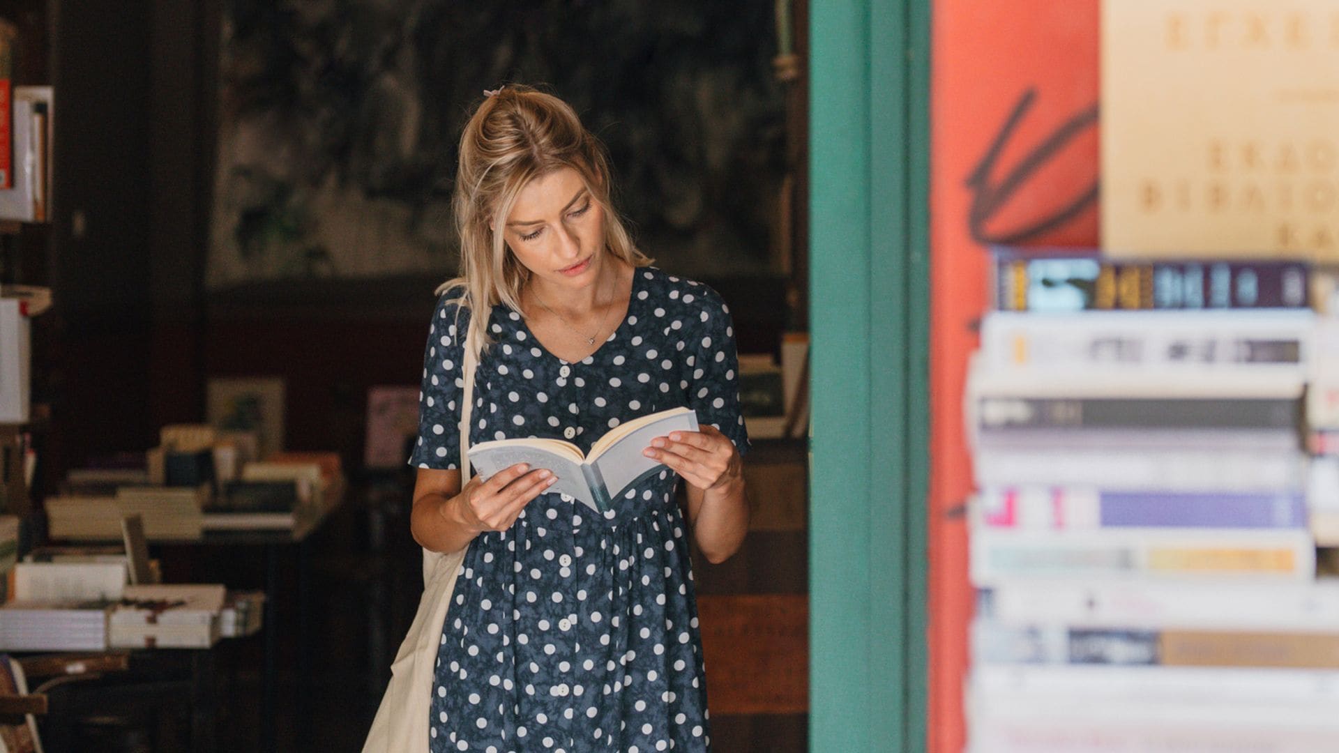 Mujer saliendo de una librería con un libro entre las manos, leyendo algunas de sus páginas.