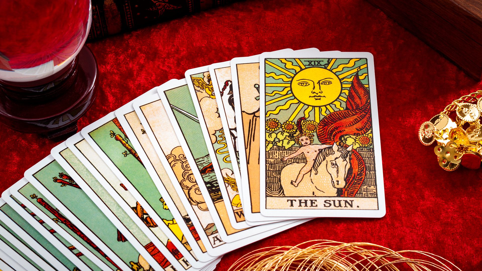 Concepto de adivinación y artesanía con cartas del tarot extendidas sobre terciopelo rojo rodeadas de una bola de cristal mágica, una pulsera de oro, un libro y una caja de madera.