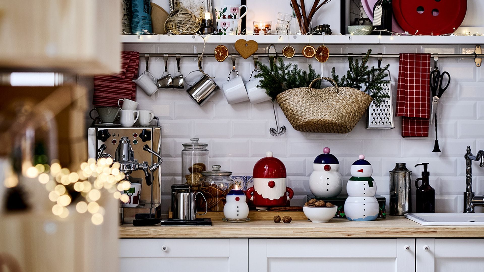 Cocina IKEA decorada con objetos navideños, muebles blancos, encimera de madera, antepecho de azulejos metro, barra de utensilios en la pared, cesto de paja 