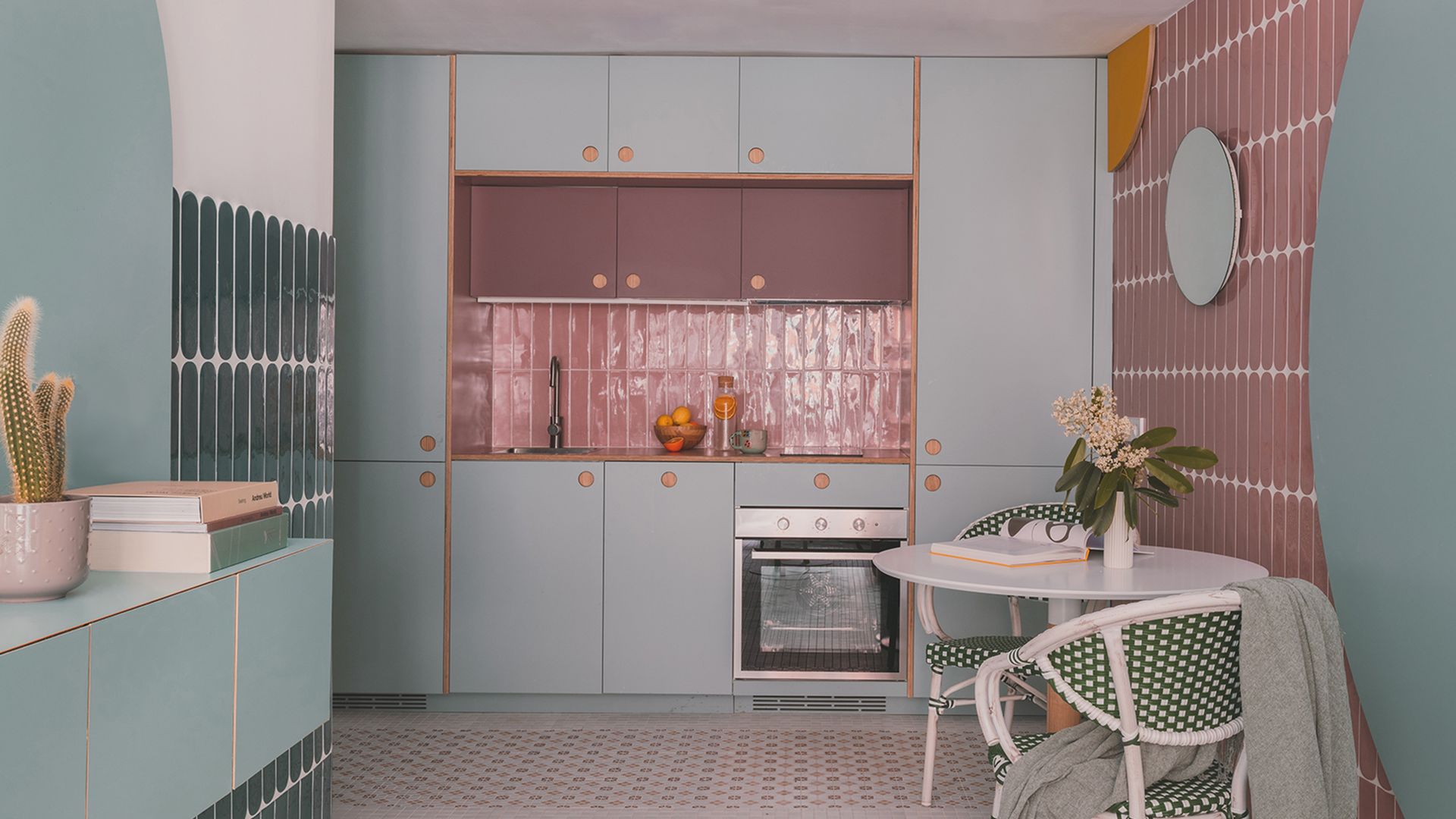Cocina con comedor con paredes de azulejos rosa claro, paneles azules, muebles de cocina azules 