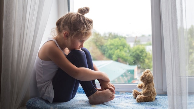 Niña triste víctima de acoso sentada en la ventana