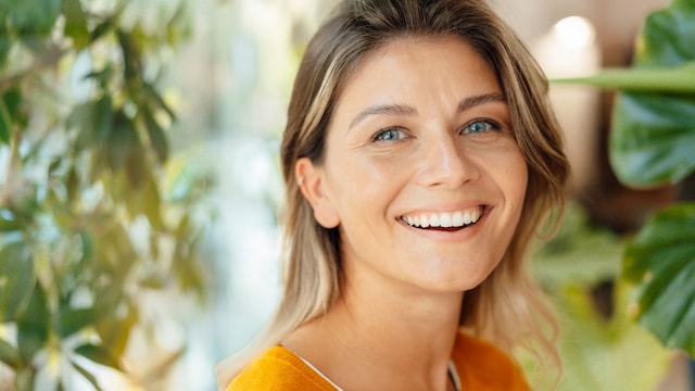 Mujer sonriendo en primer plano con cabello rubio y ojos azules, sonrisa.