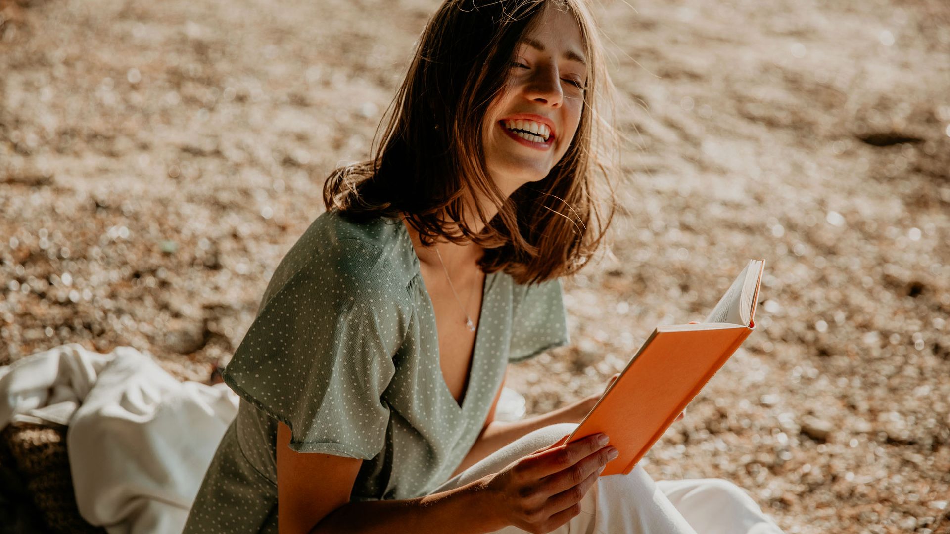 Mujer riendo leyendo un libro en la arena