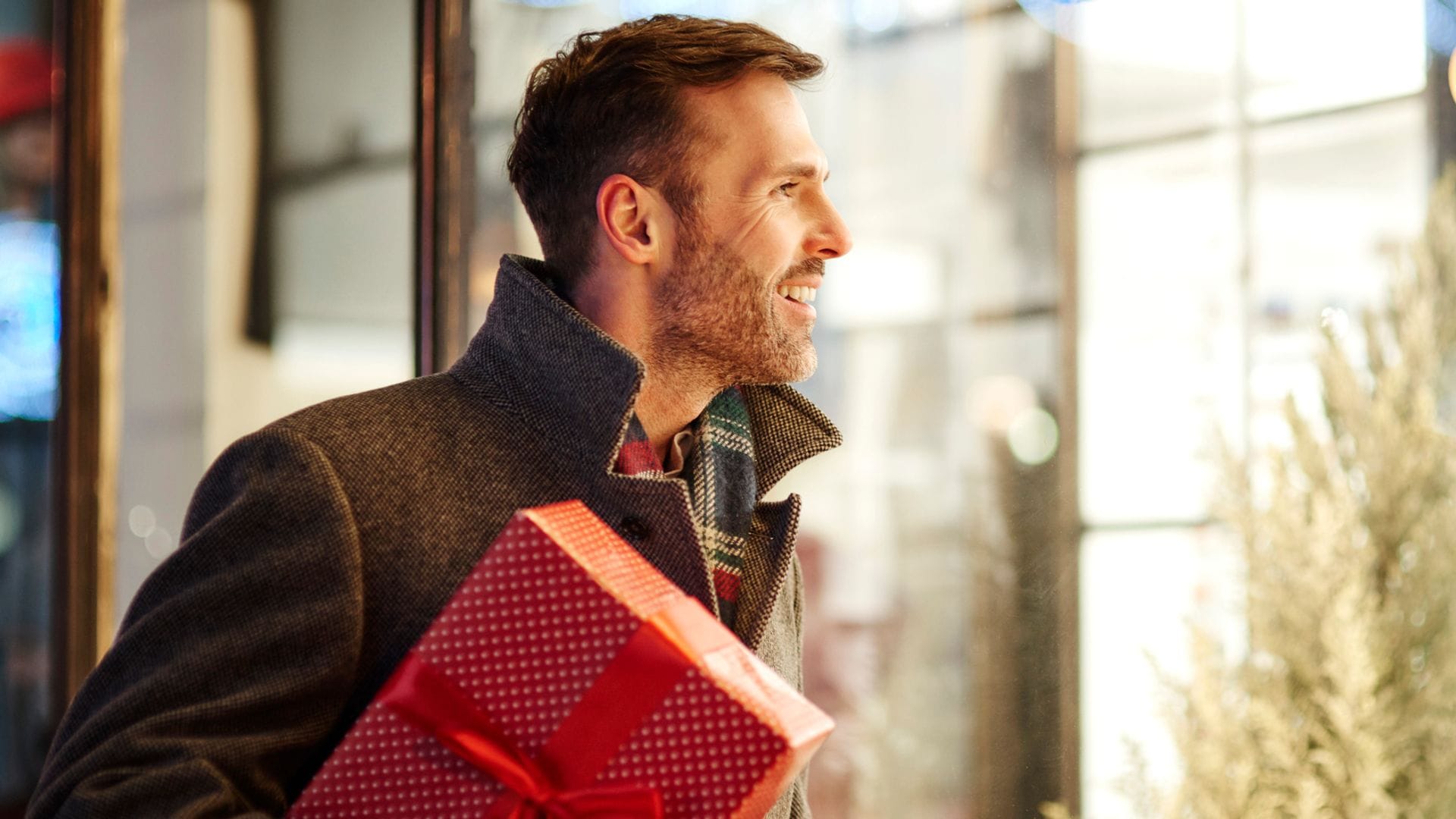 Hombre sonriente en la calle mirando escaparates con regalo en la mano