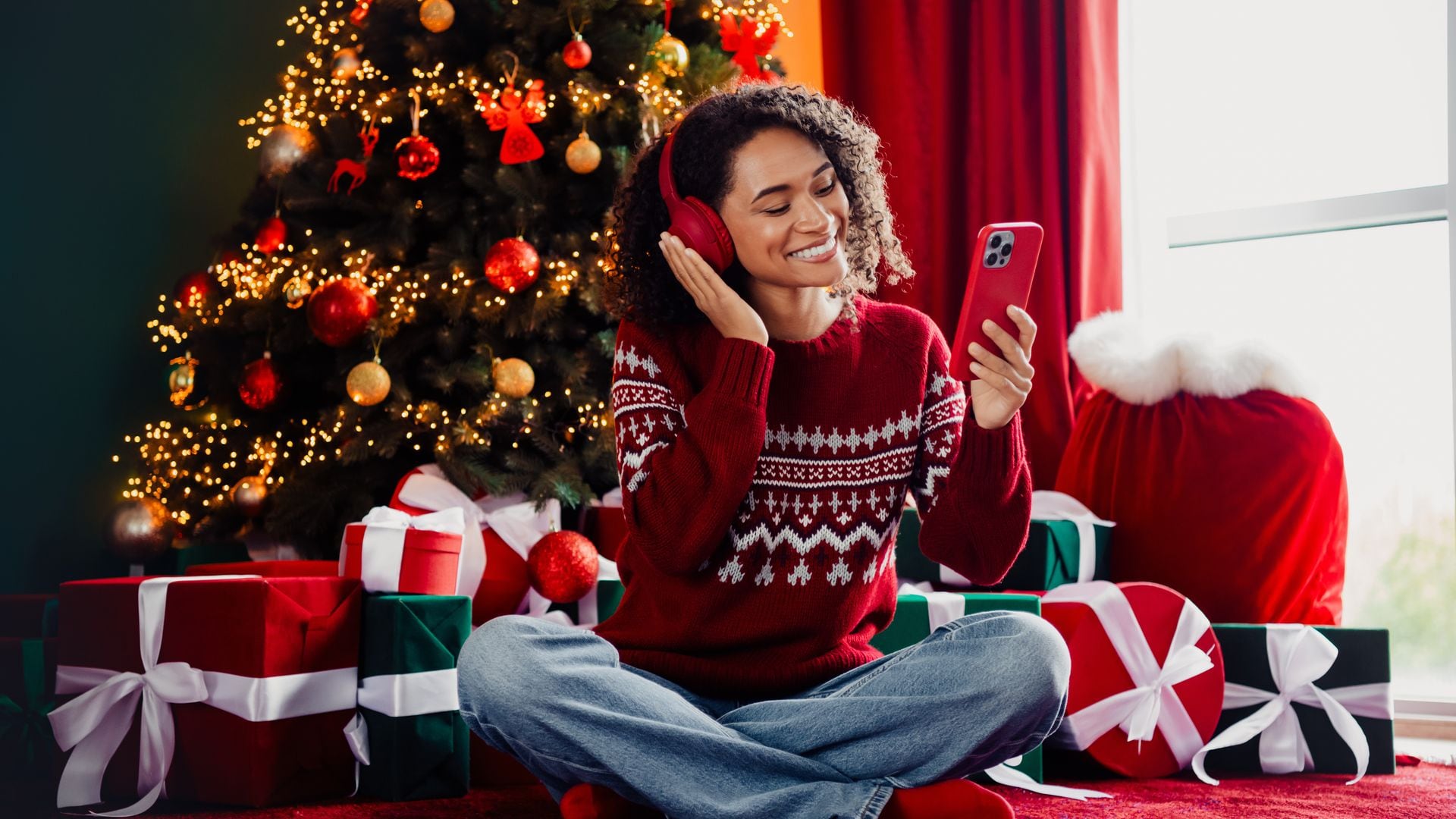 mujer con auriculares, escuchando música junto al árbol de Navidad y rodeada de regalos
