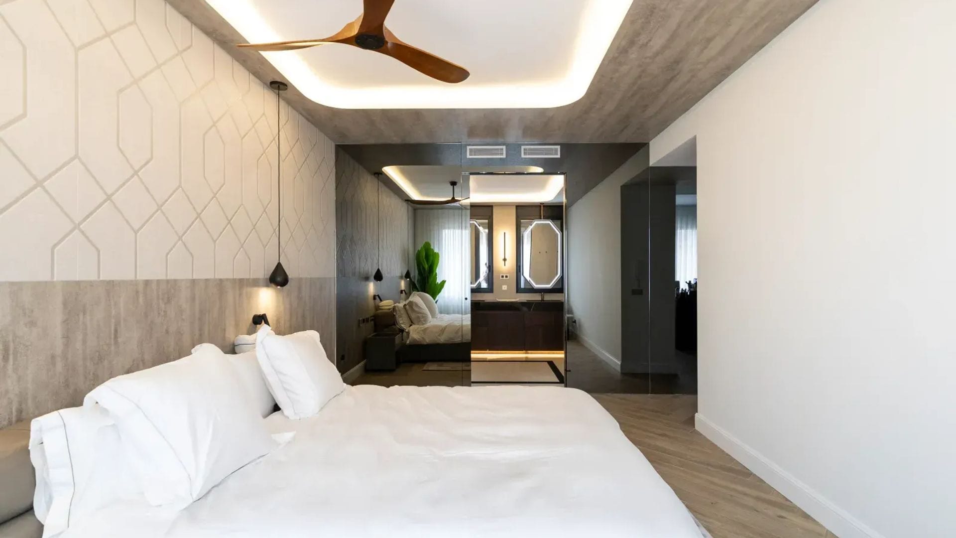 Dormitorio con pared del cabecero decorada, ventilador de techo, pared de espejo, baño integrado